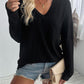 Woman wearing Double Take Pocketed Textured V-Neck Long Sleeve T-Shirt with denim shorts and holding a beige clutch.