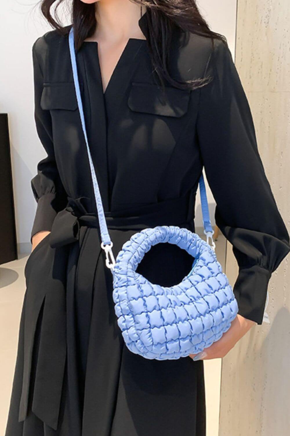 Woman holding Bella Road quilted puffy crossbody bag with removable strap, styled as a clutch, in a fashionable setting.