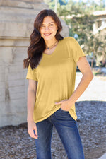 Woman wearing Basic Bae Bamboo Full Size V-Neck Short Sleeve T-Shirt in yellow, standing outdoors, smiling, with hand in pocket