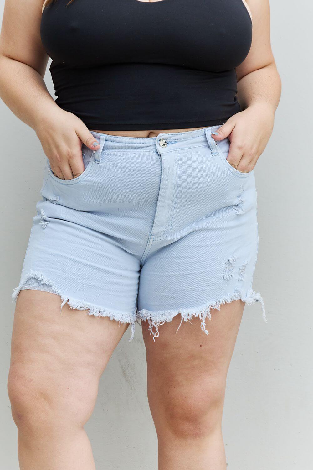 Woman wearing Katie High Waisted Distressed Shorts in Ice Blue by Risen Jeans, showcasing trendy style and comfortable fit