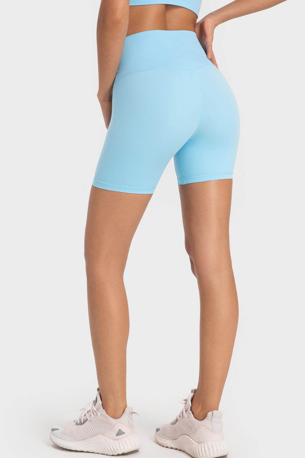 Back view of a woman wearing light blue Millennia Staying Cozy biker shorts with a wide waistband and sporty style.