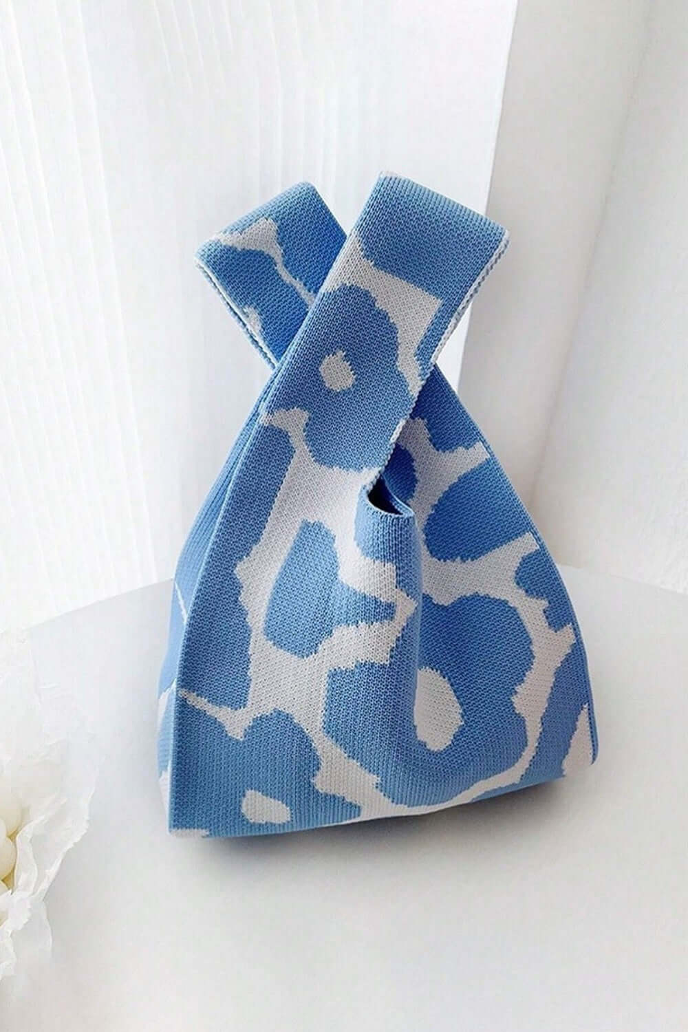 Eco-friendly blue and white flower-pattern knitted handbag with unique knot design on a white background.