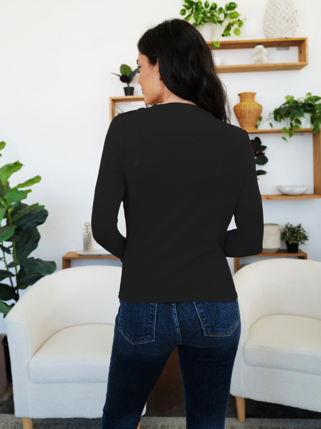 Woman wearing black long sleeve T-shirt standing in stylish living room with green plants and modern decor.