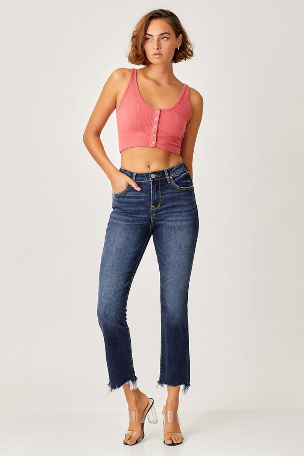 Woman wearing Risen Jeans frayed hem cropped straight jeans paired with a coral crop top and clear heels for a chic casual look.