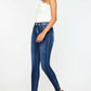 Woman modeling Kancan high-rise ankle skinny jeans with stylish double waistband and release hem in dark wash, paired with black heels.