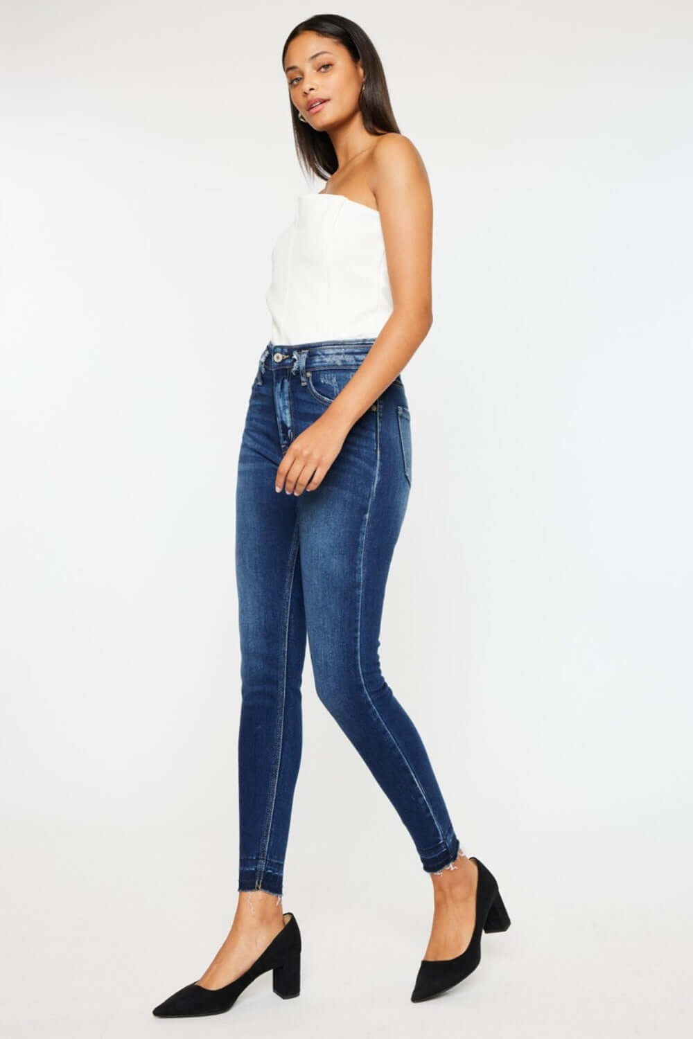 Woman modeling Kancan high-rise ankle skinny jeans with stylish double waistband and release hem in dark wash, paired with black heels.