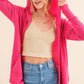 Woman wearing pink thermal hooded open front cardigan with pockets styled over a beige tank top and blue jeans.