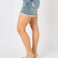 Woman wearing Button Fly Raw Hem Denim Shorts by Judy Blue Jeans, showing side view. Trendy, high-quality denim shorts perfect for casual outfits.