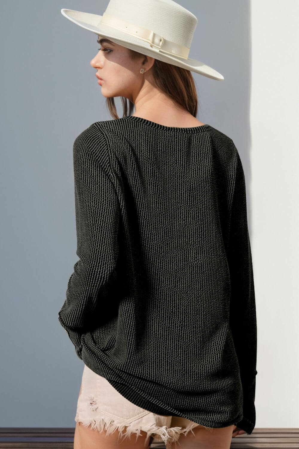 Woman wearing black Double Take Full Size Notched Thumbhole Long Sleeve T-Shirt with beige hat and shorts, viewed from back.