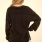 Back view of a woman wearing the VERY J Washed V-Neck Exposed Seam Knit Top in black with drop shoulder and long sleeves.