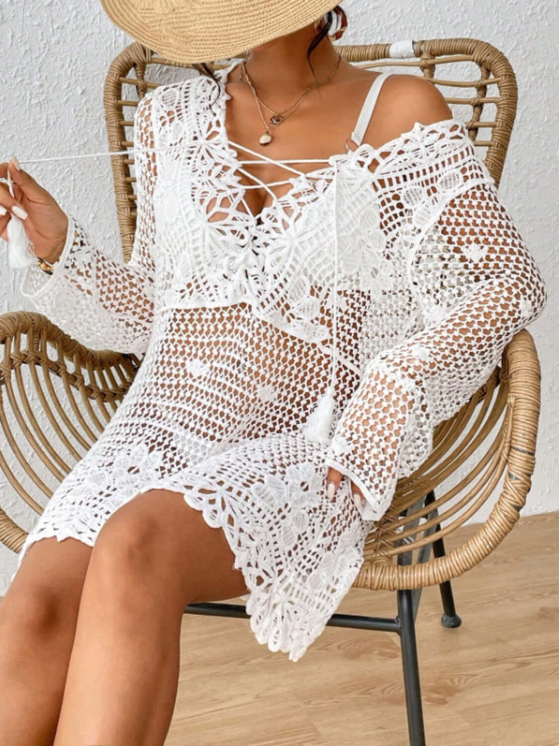 Woman wearing a Cutout Tied V-Neck Long Sleeve Cover Up in white crochet design, sitting on a wooden chair