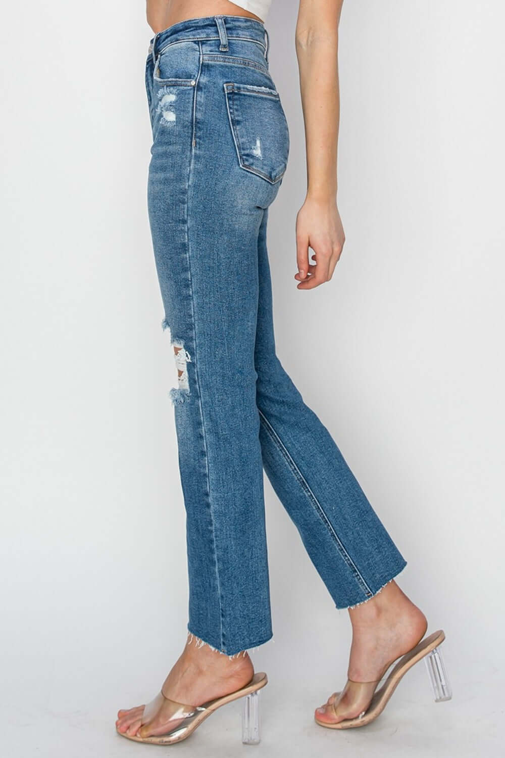 Side view of high rise distressed ankle jeans by Risen Jeans styled with clear heels.