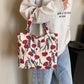 Printed canvas medium handbag with zipper, featuring red and green floral design carried by person in casual outfit.