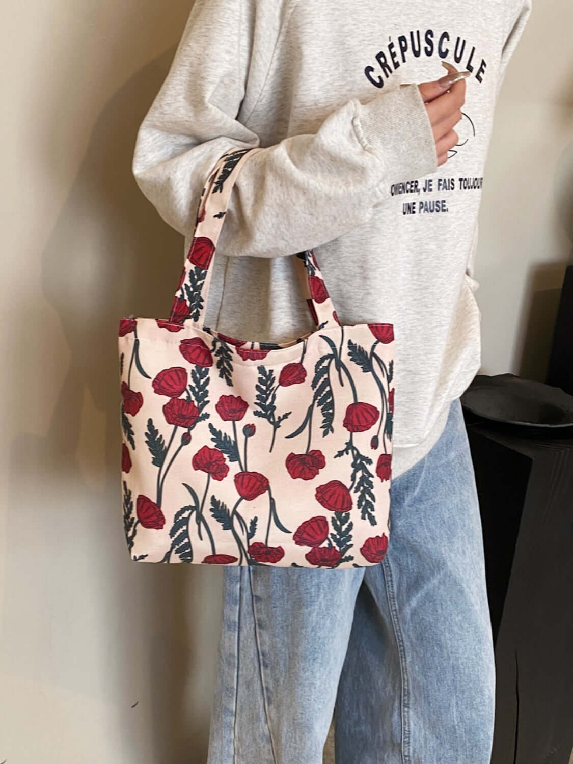 Printed canvas medium handbag with zipper, featuring red and green floral design carried by person in casual outfit.