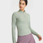 Millennia Half Zip Thumbhole Sleeve Sports Top in soft green, paired with purple shorts, perfect for workouts.