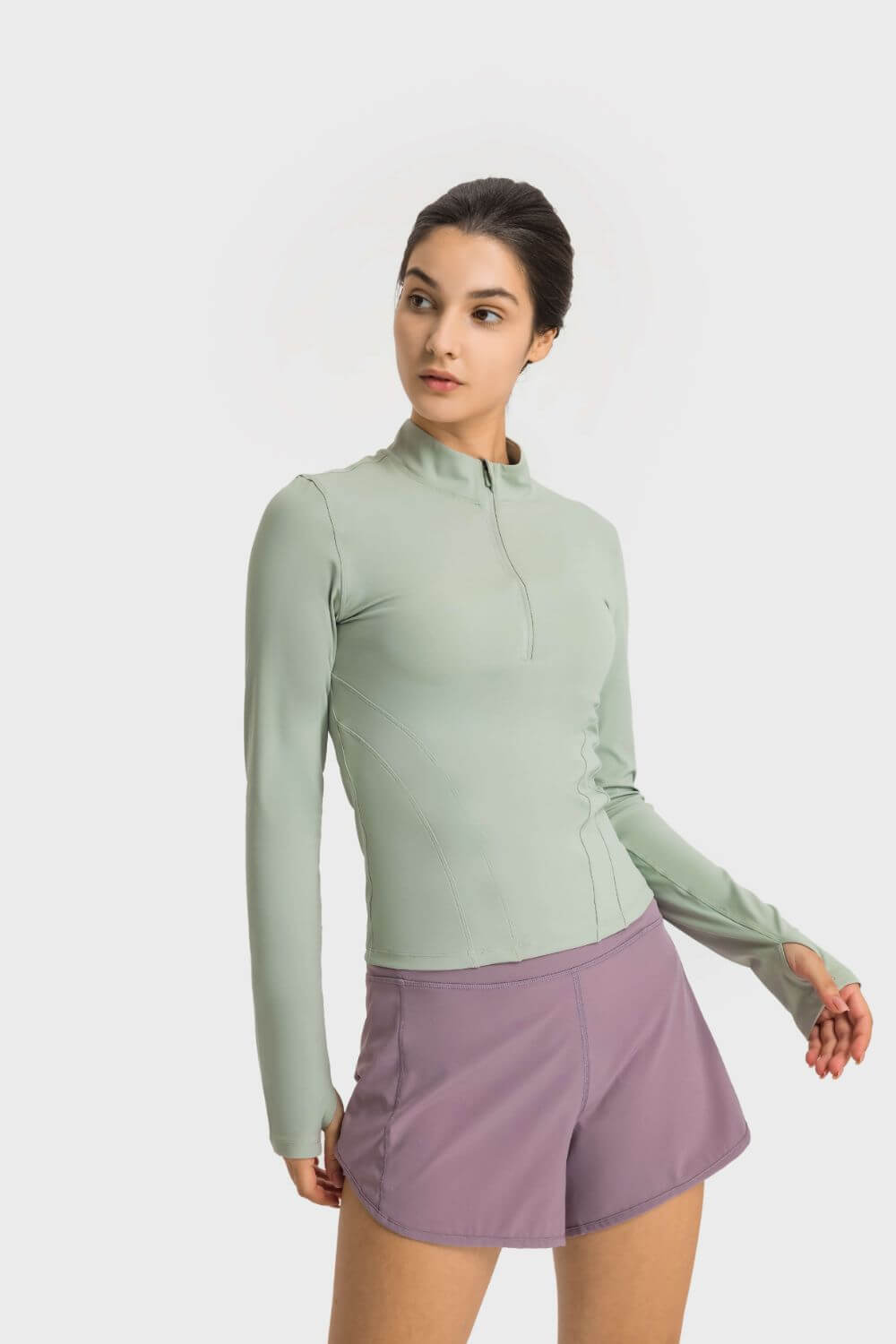 Millennia Half Zip Thumbhole Sleeve Sports Top in soft green, paired with purple shorts, perfect for workouts.