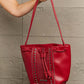 Red Nicole Lee USA Amy Studded Bucket Bag with drawstring and snap button closure held by hand.