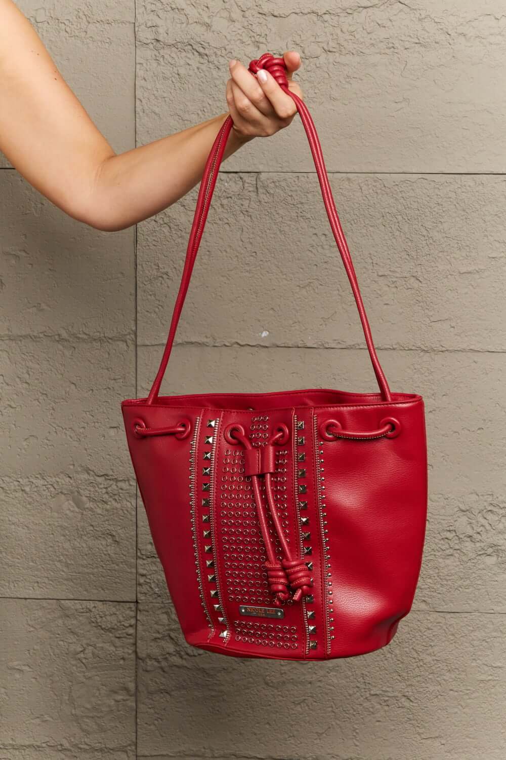 Red Nicole Lee USA Amy Studded Bucket Bag with drawstring and snap button closure held by hand.