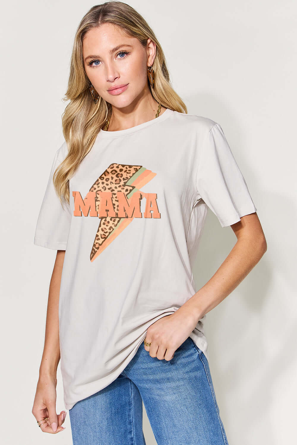 Woman wearing a MAMA Round Neck Short Sleeve T-Shirt with graphic design, paired with blue jeans