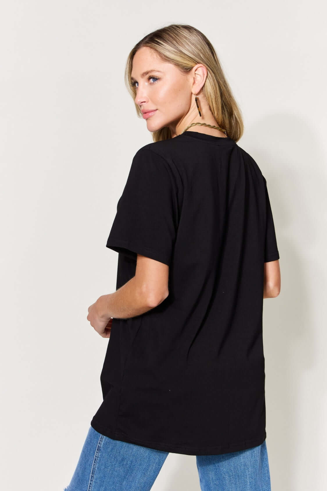 Woman wearing black graphic round neck short sleeve t-shirt with blue jeans, back view.