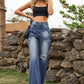 Woman wearing Bella Road Distressed Jeans with stylish pockets in navy, paired with a black top, standing outdoors near a stone wall.