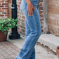 Woman wearing Pearl Trim High Waist Bootcut Jeans in blue, featuring a stylish pearl trim along the sides, standing outdoors.