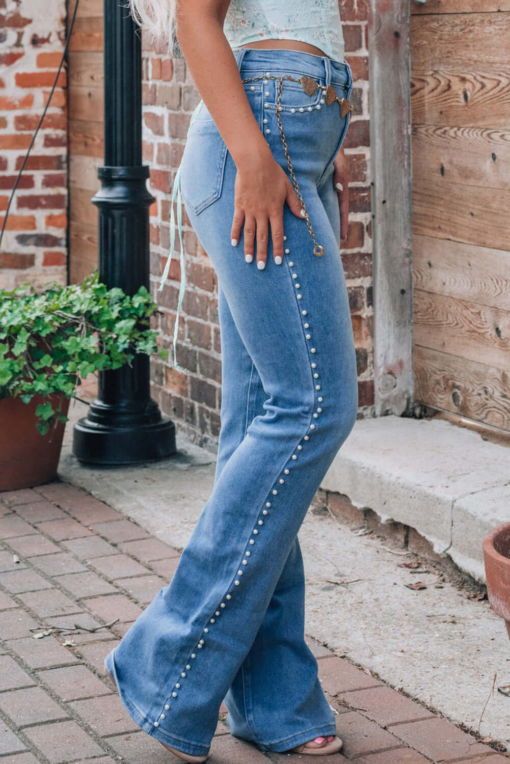 Woman wearing Pearl Trim High Waist Bootcut Jeans in blue, featuring a stylish pearl trim along the sides, standing outdoors.