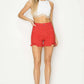 Model wearing high rise distressed red denim shorts from Risen Jeans with a white crop top.