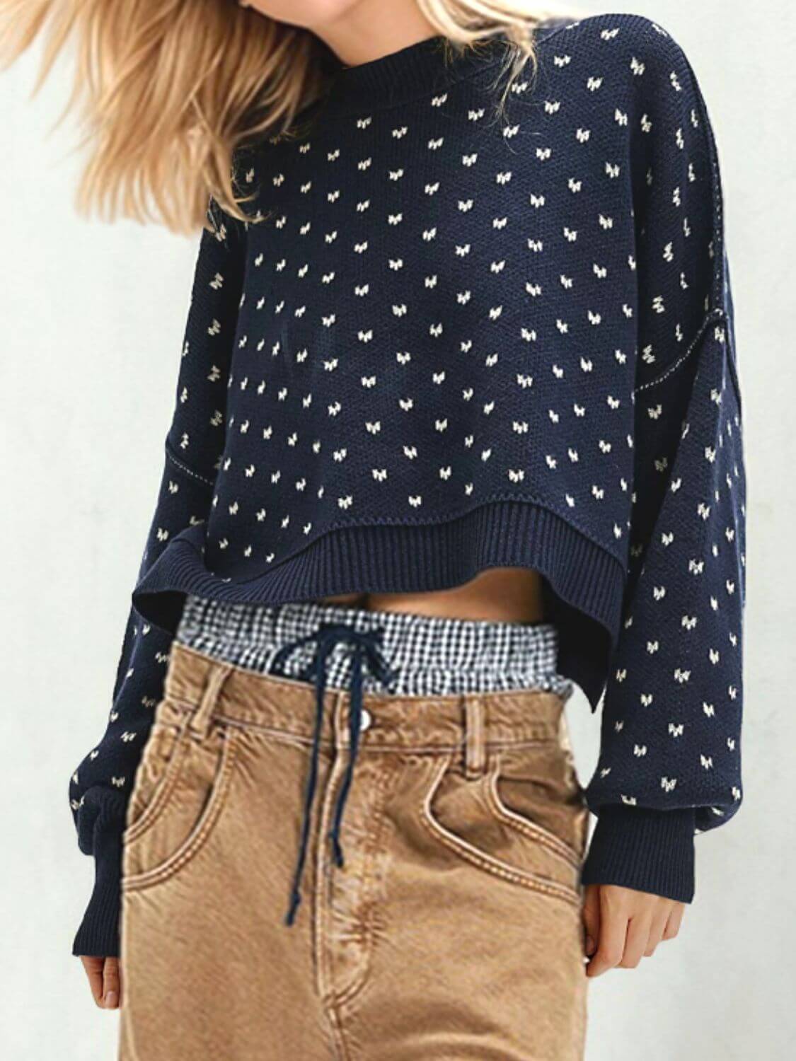 Woman wearing a navy sweater with white patterns and long sleeves, paired with beige trousers for a cozy fall look.