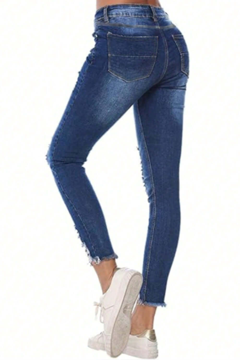 Woman wearing distressed raw hem jeans with pockets, showcasing back view and paired with white sneakers.