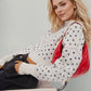 Stylish woman wearing a cozy white sweater with black patterns and holding a red bag, seated comfortably.