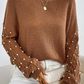 Bella Road Pearl Detail Round Neck Long Sleeve Sweater in brown, showcasing elegant pearl detailing on sleeves, worn with white pants.