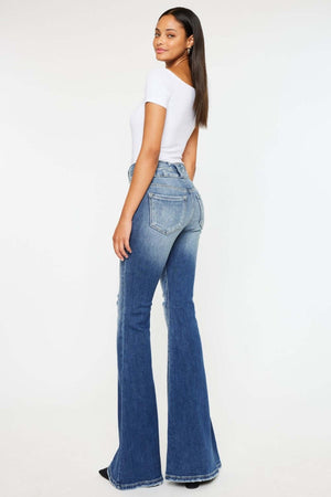 Woman wearing Kancan high-rise flare jeans in dark stone wash with distressed detailing and raw hem, styled with a fitted white top.