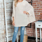 Woman wearing Bella Road Round Neck Batwing Sleeve Sweater with ripped jeans, standing in a cozy room.