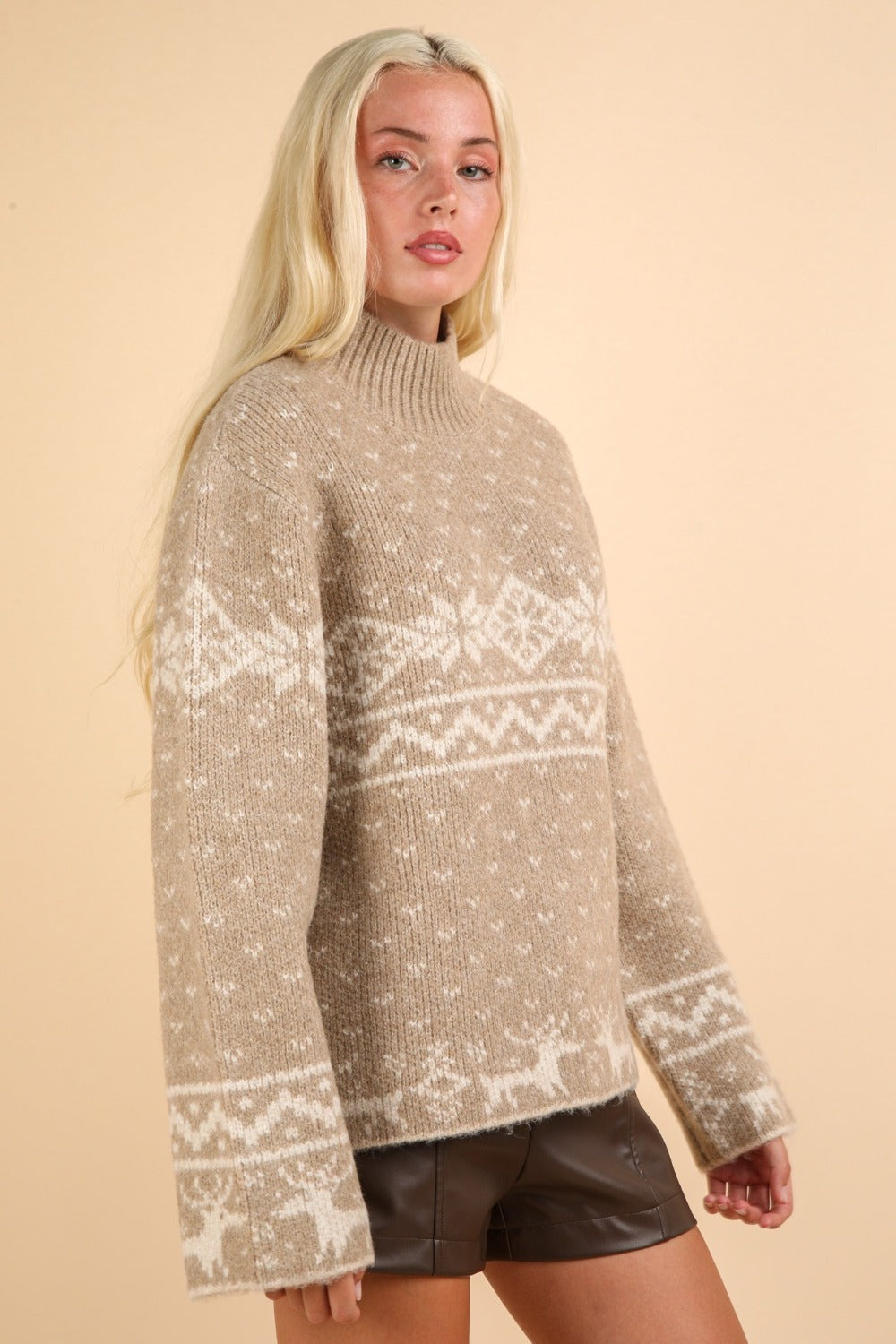 Woman wearing beige Christmas element mock neck long sleeve sweater with festive reindeer and snowflake patterns.