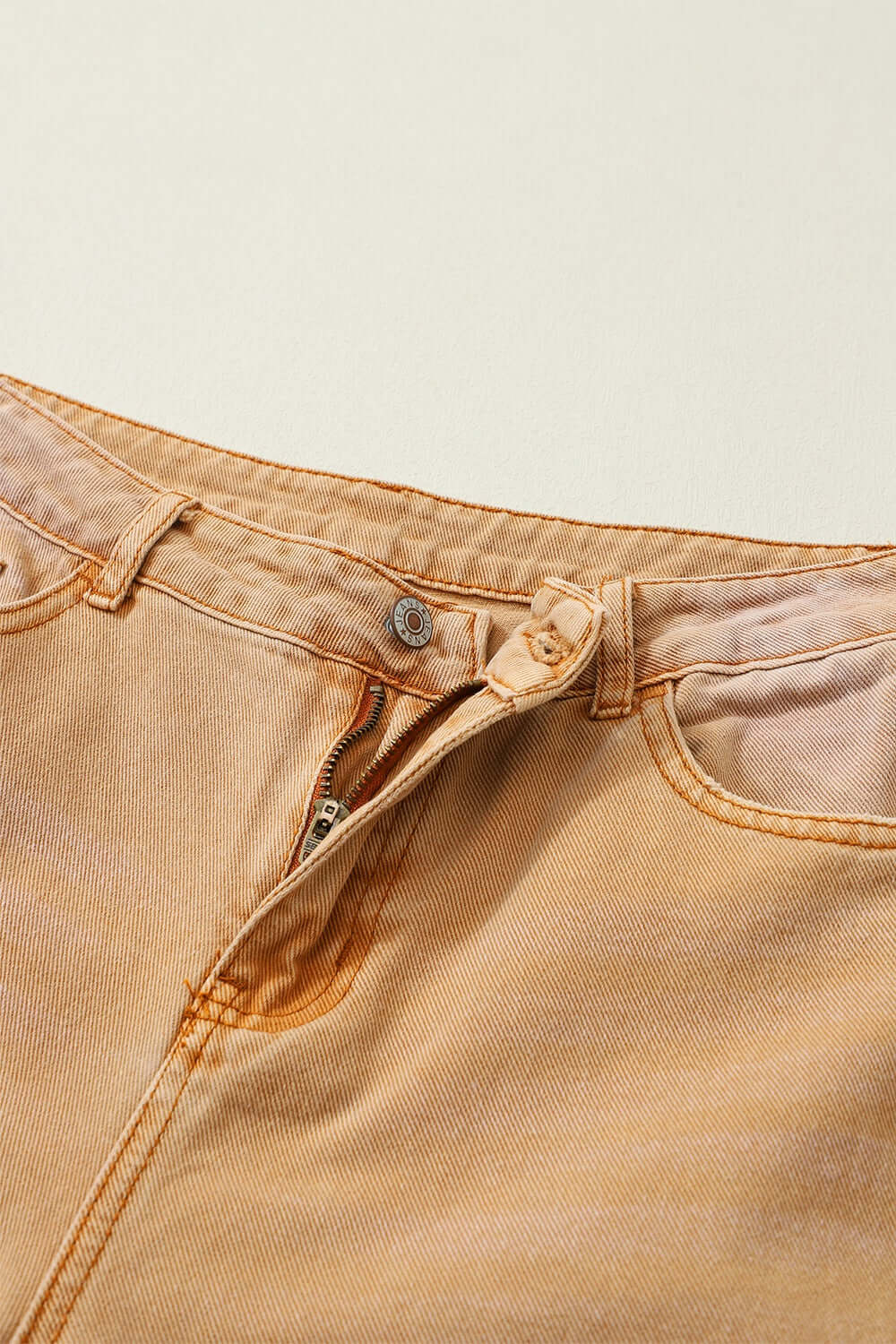 Close-up of Distressed Raw Hem Jeans with Pockets showcasing the top button and zipper detail in light beige color.