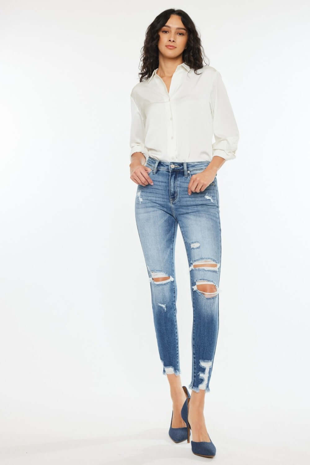 High Rise Frayed Ankle Skinny Jeans in medium wash with distressed detailing and stretch denim, worn by a woman in a white shirt and heels.