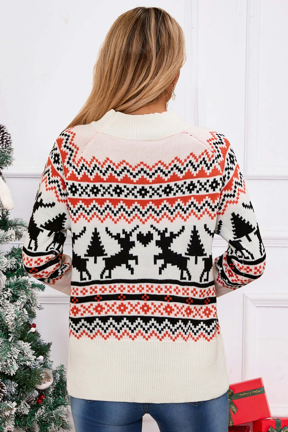 Woman wearing a cozy sweater with reindeer and angel wing design near a festive Christmas tree, perfect for holiday cheer.