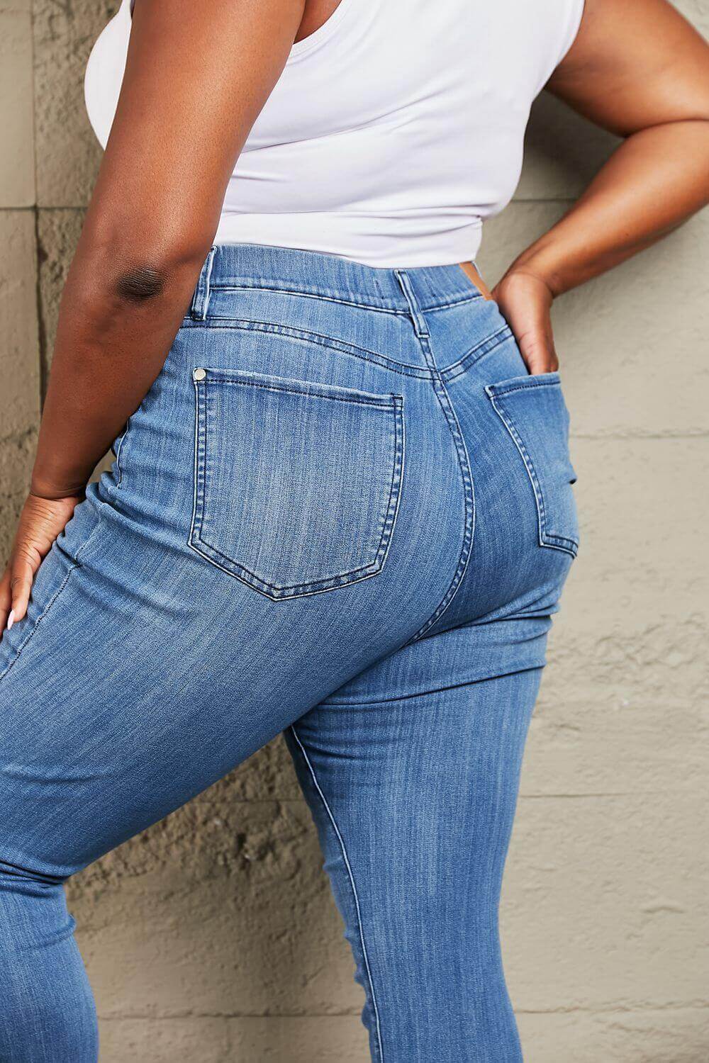 Woman wearing Janavie full-size high waisted pull on skinny jeans with release hem detailing, showcasing back view. Judy Blue Jeans.