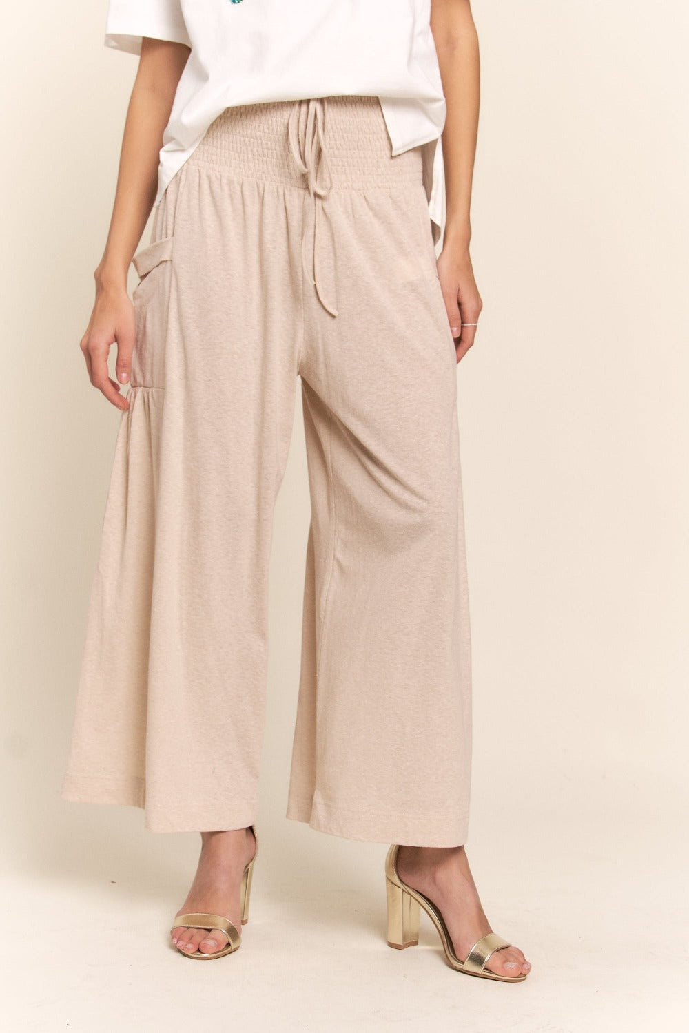 Woman wearing J.NNA smocked waist boho wide leg pants with pockets, showcasing stylish and comfortable fit.