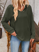 Woman wearing a drawstring dropped shoulder long sleeve hoodie in dark green paired with blue jeans.