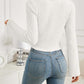 Woman in Bella Road Ribbed Drawstring Long Sleeve T-Shirt, white, back view, paired with blue jeans in a well-decorated room.