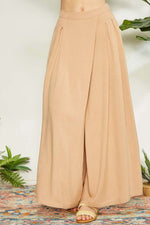 Wide leg pants with wrap pleating detail in beige, showcased with a chic design on a colorful textured floor.