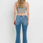 Woman wearing mid-rise distressed cropped flare jeans with a back view, showcasing trendy and edgy denim details.