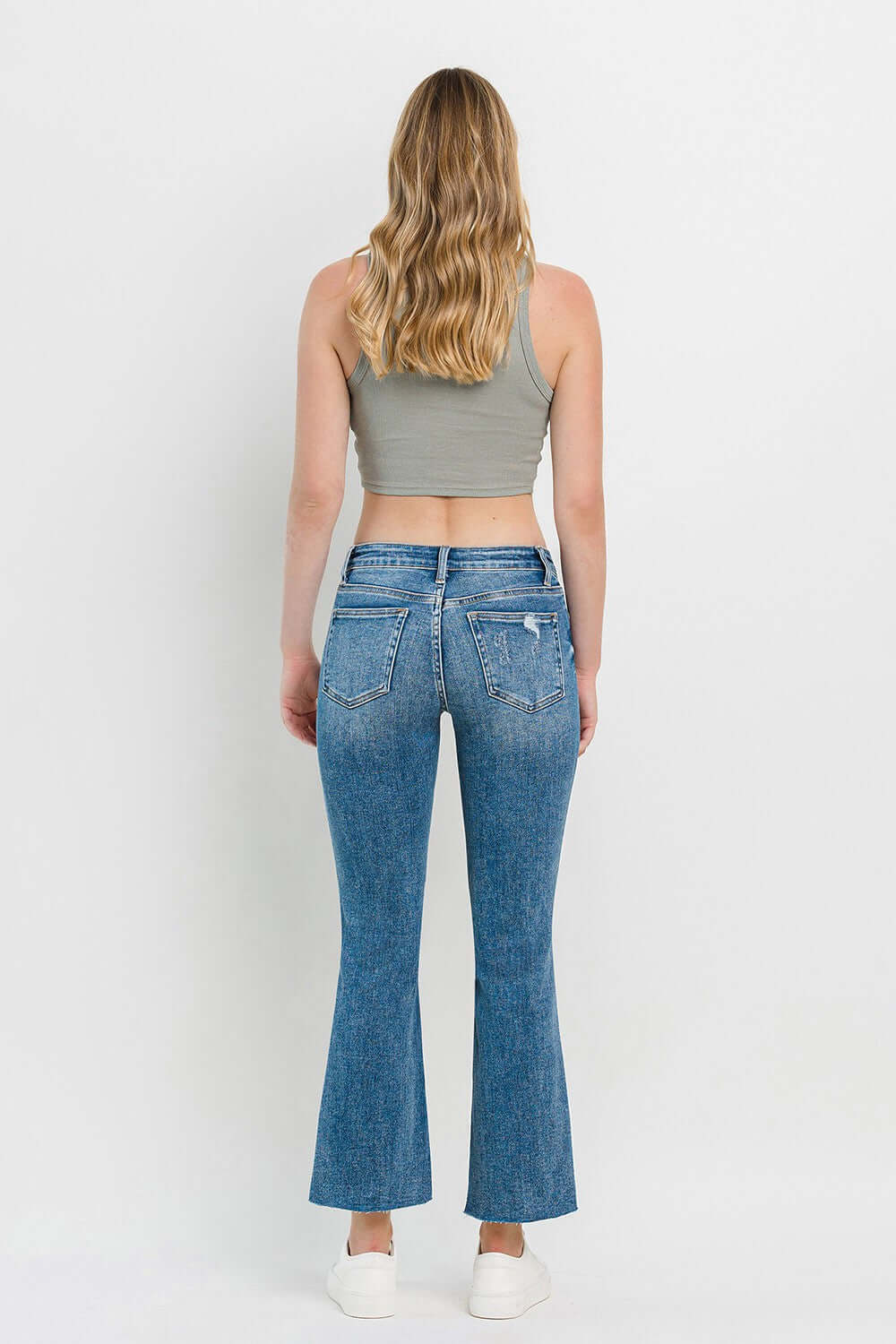 Woman wearing mid-rise distressed cropped flare jeans with a back view, showcasing trendy and edgy denim details.