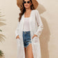 Woman wearing a lace detail open front long sleeve cover-up over denim shorts and a tank top, accessorized with a sunhat and sunglasses.