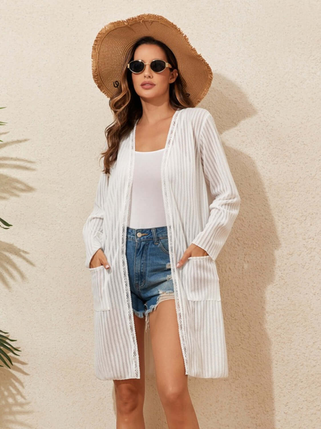 Woman wearing a lace detail open front long sleeve cover-up over denim shorts and a tank top, accessorized with a sunhat and sunglasses.