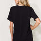 Back view of woman wearing black MAMA round neck short sleeve T-shirt, paired with blue jeans.