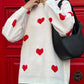 Woman wearing Bella Road Heart Round Neck Dropped Shoulder Sweater with red heart detailing and holding a black handbag in front of red door