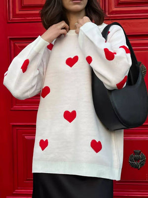 Woman wearing Bella Road Heart Round Neck Dropped Shoulder Sweater with red heart detailing and holding a black handbag in front of red door